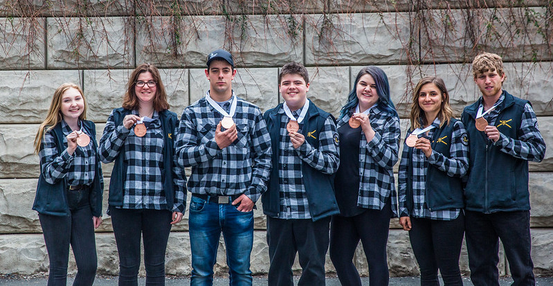 7 members of Team Nova Scotia display their winning medals against a brick background.